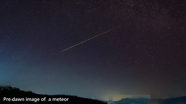 A bright meteor passing through the sky in the early morning before sunrise